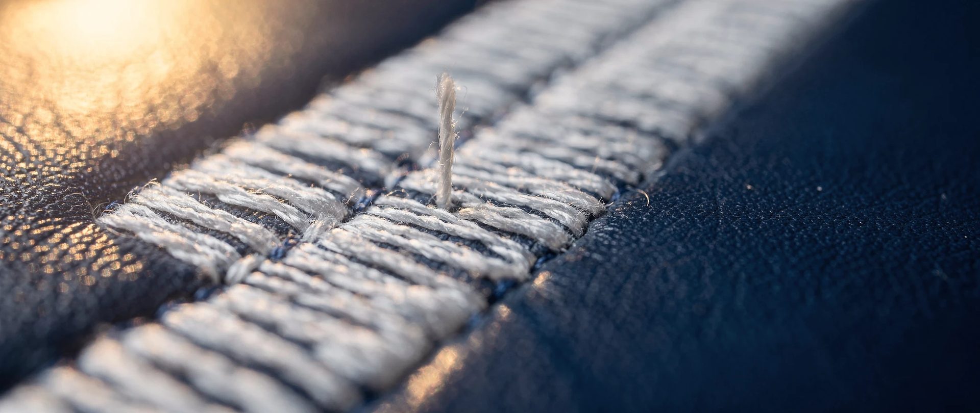 Broderie dense au fil blanc sur cuir bleu marine brillant, avec un fil qui se soulève.
