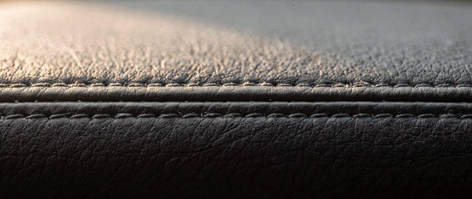 Double rangée de piqûres nettes sur un cuir gris foncé, avec de petits plis où deux coutures se croisent.
