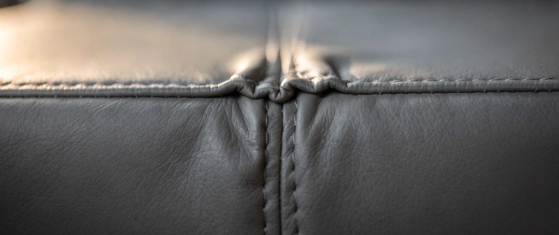 Cuir gris avec des plis de tension le long d'une couture que le rembourrage ne remplit pas.