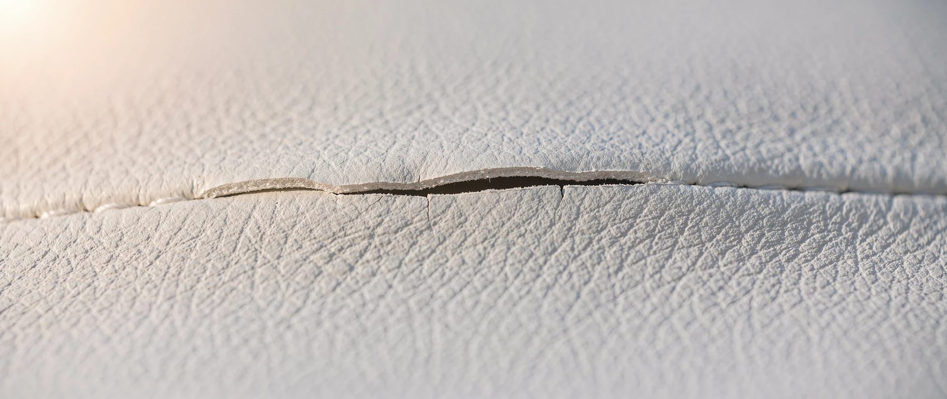 Vinyle marin blanc au grain fin traversé d'une fissure le long d'une couture.