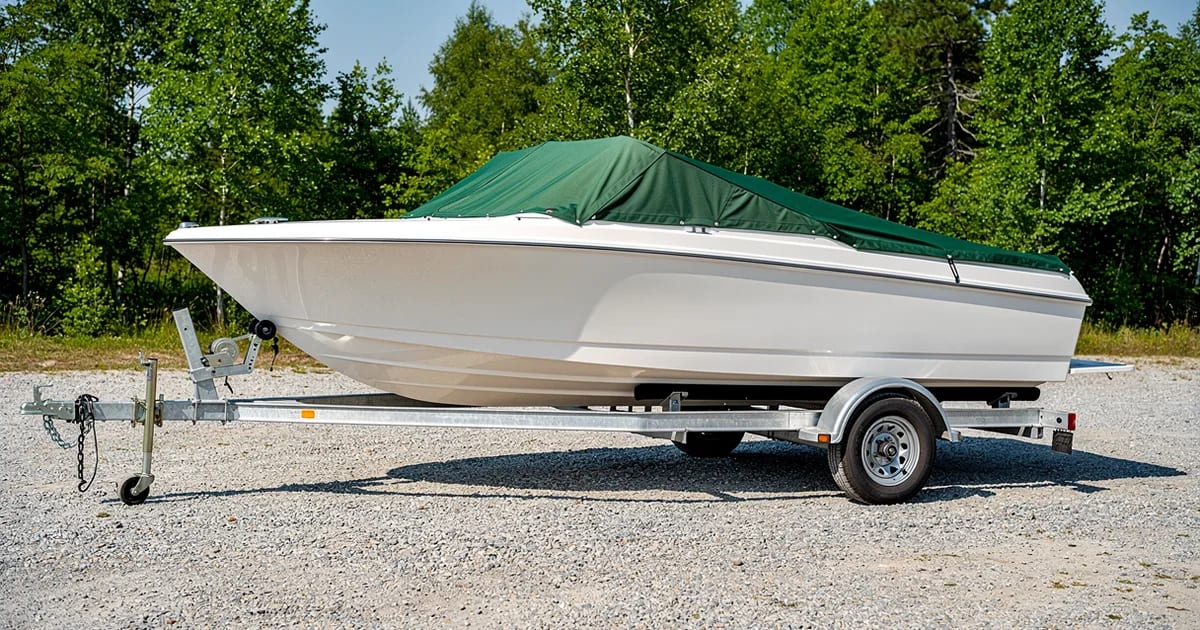 Bateau sur remorque en plein soleil avec une toile verte légèrement pâlie, un exemple de la durée de vie d'une toile de bateau au Québec.